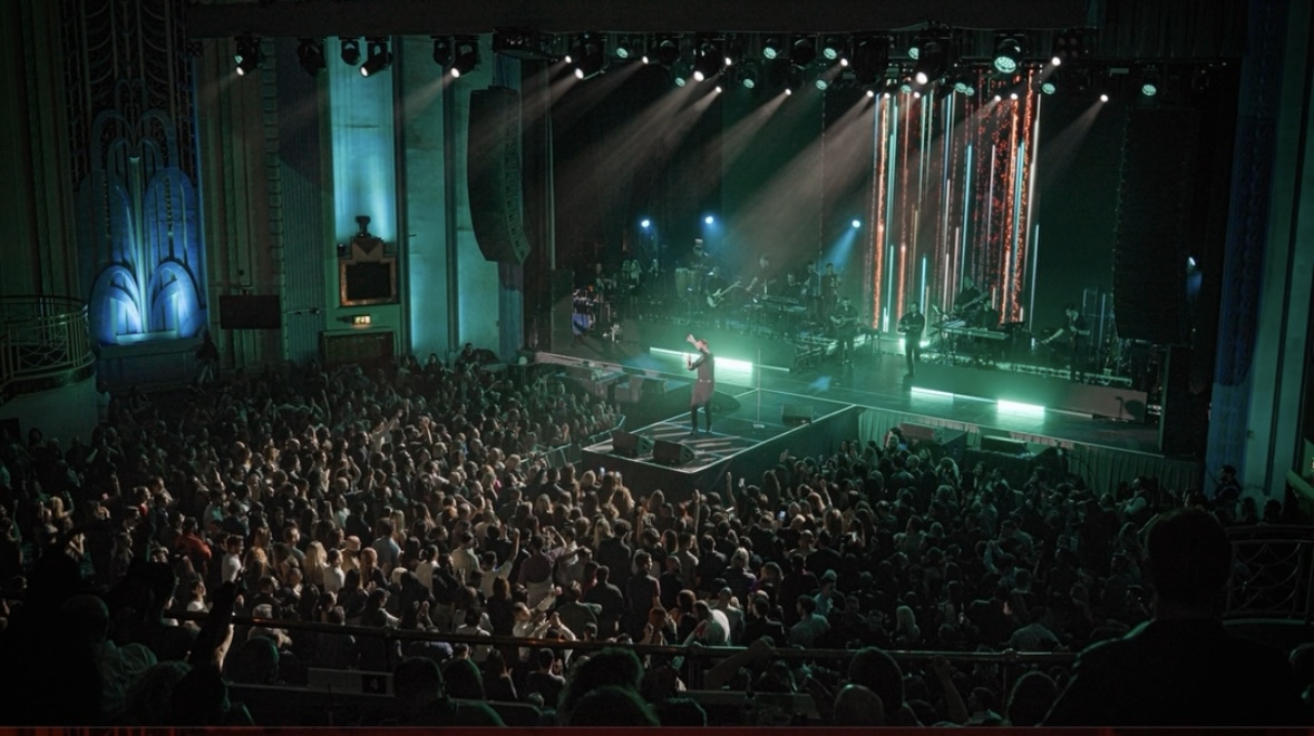 A packed concert audience beneath green stage lights