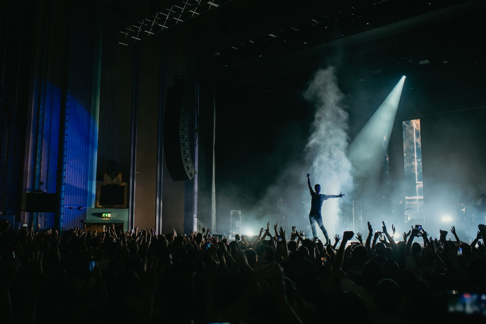 A performer under white spotlights, with hands raised in the crowd