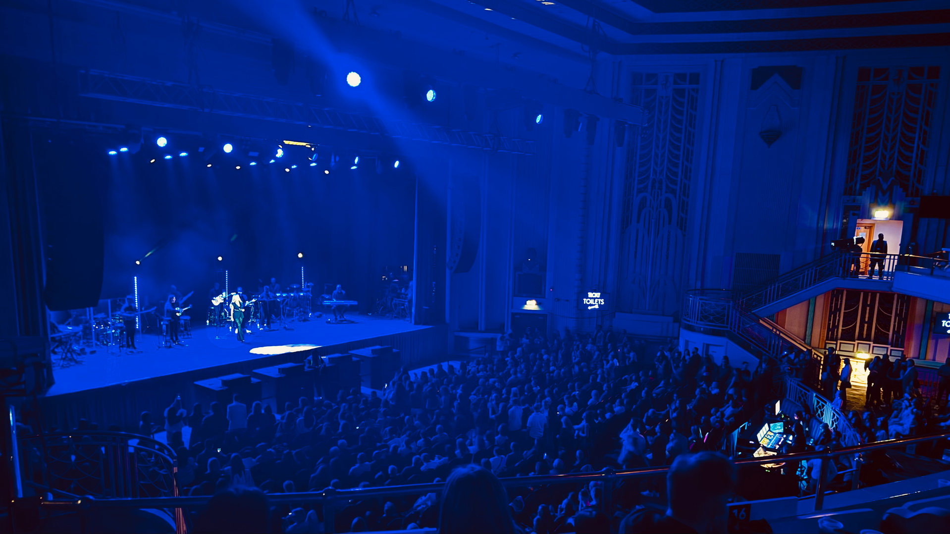 A wide view of the Troxy audience and blue-lit stage from the balcony
